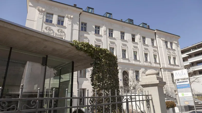 Historisches Gebäude mit moderner Glasfassade im Vordergrund und Dachfenstern unter blauem Himmel.