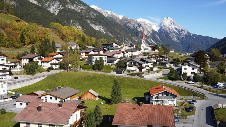 Dorf in einem Tal mit schneebedeckten Bergen und vielen Häusern unter blauem Himmel.