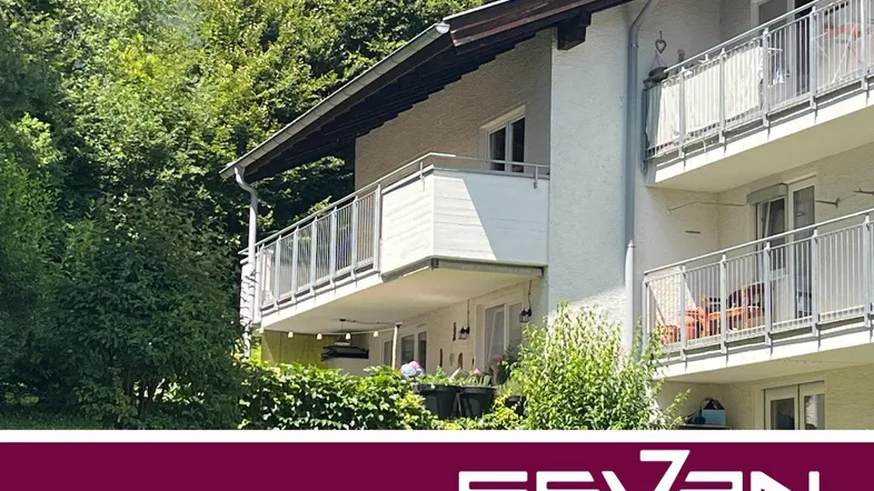 Mehrfamilienhaus mit mehreren Balkonen, umgeben von üppigem Grün und Bäumen.