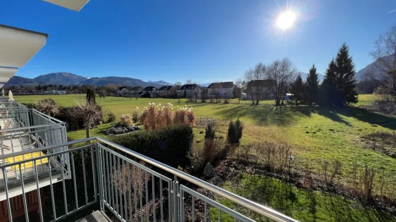 Sonniger Balkon mit weitem Blick über grüne Felder und die umliegende Berglandschaft.