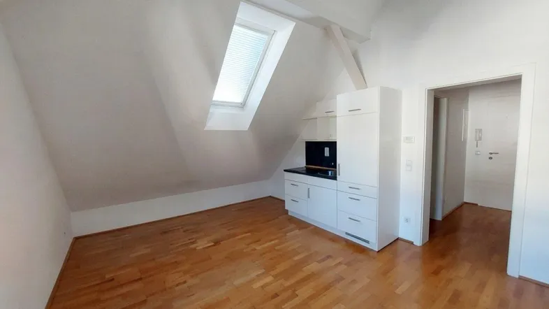 Helles Dachzimmer mit Holzboden, Dachfenster und einer kompakten, integrierten Küchenzeile.