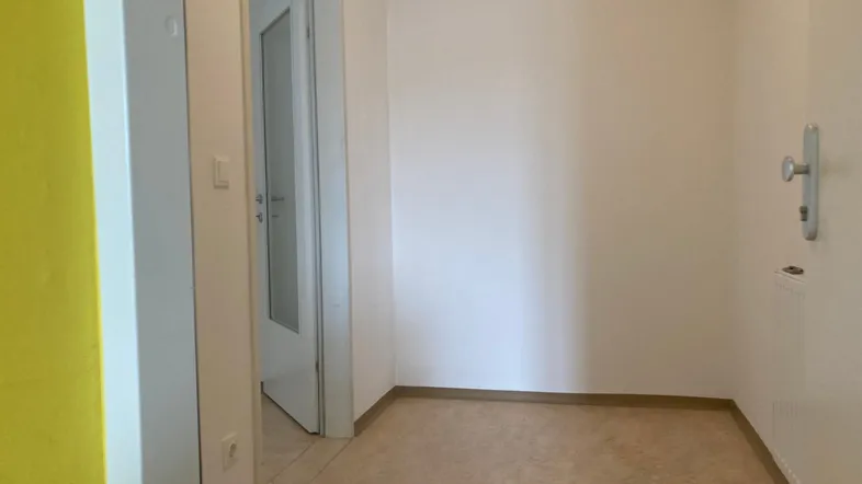 Heller Eingangsbereich mit weiß gestrichenen Wänden und einem gelben Akzentbereich.