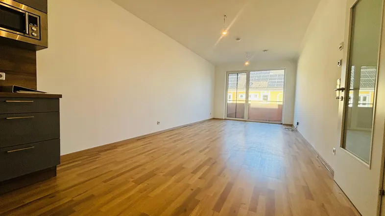 Heller offener Wohnbereich mit Parkettboden und Zugang zu einem Balkon, ideal für entspannte Stunden.