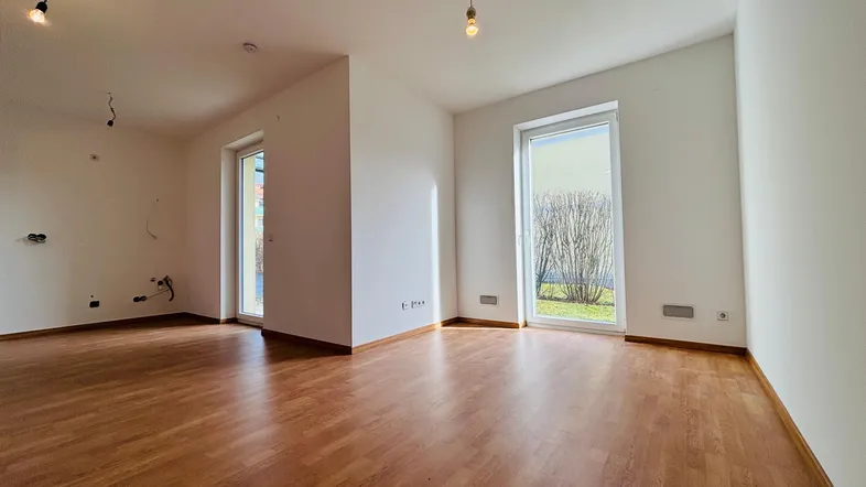 Heller, leerer Raum mit Holzboden und großen Fenstern, die viel Tageslicht hereinlassen.