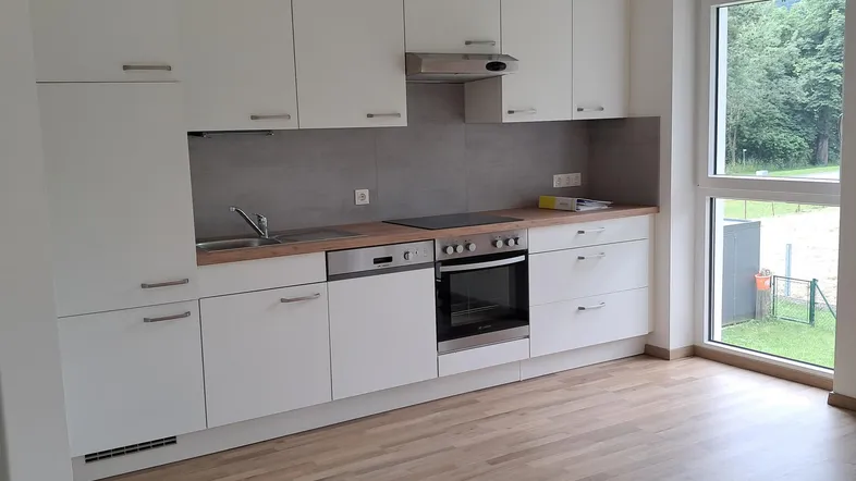 Moderne Einbauküche mit weißen Schränken, Holzarbeitsplatte und Blick ins Grüne.