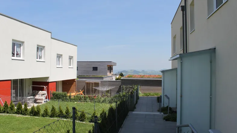 Moderne Reihenhäuser mit gepflegten Gärten und einem Weg, der zu weiteren Gebäuden führt.