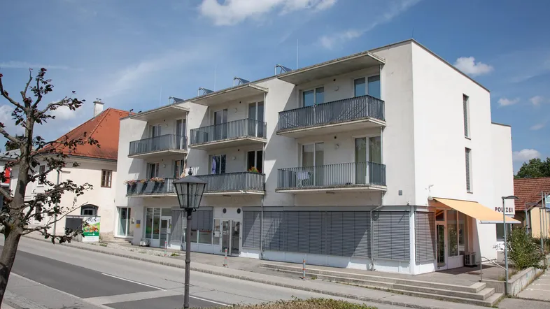 Modernes Mehrfamilienhaus mit mehreren Balkonen und Geschäften im Erdgeschoss an einer Straße gelegen.