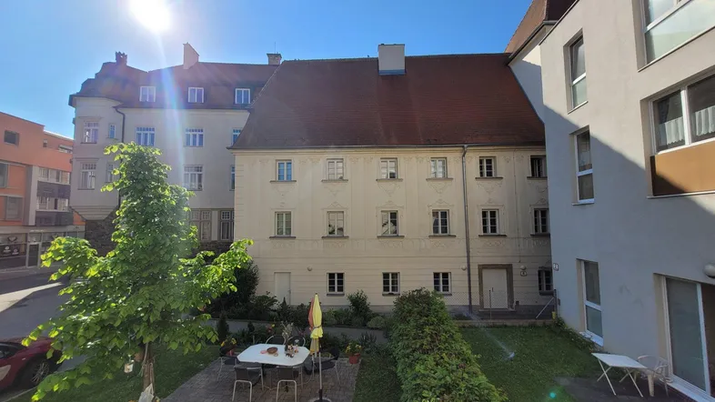 Sonniger Innenhof mit gepflegtem Gartenbereich, Sitzgelegenheiten und Blick auf historische Gebäude.