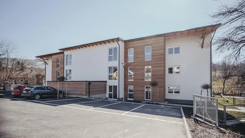 Modernes Wohngebäude mit Holzfassadenelementen und Parkplätzen unter strahlend blauem Himmel.