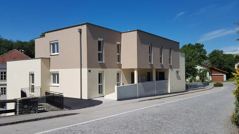 Modernes Mehrfamilienhaus mit zweifarbiger Fassade und klaren Linien in sonniger Lage.