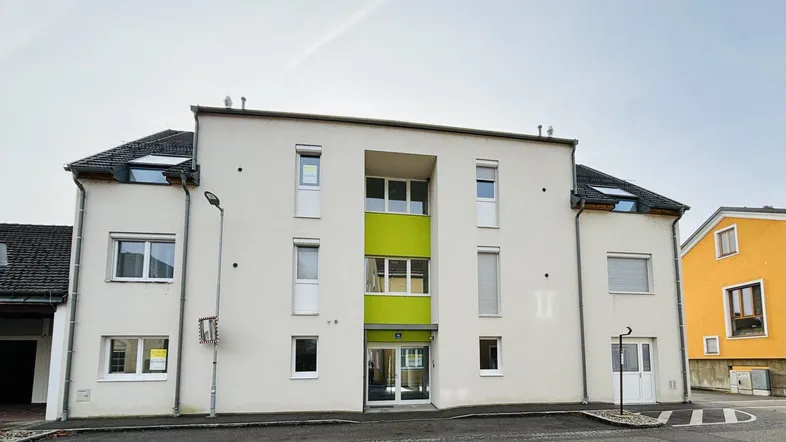 Modernes Mehrfamilienhaus mit weißer Fassade und grünen Akzenten an der Vorderseite.