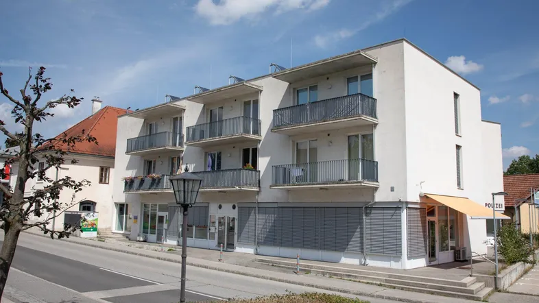 Modernes Mehrfamilienhaus mit Balkonen und Geschäften im Erdgeschoss an einer Straße.