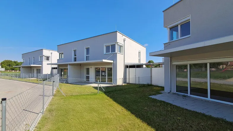 Moderne Reihenhäuser mit schlichter Fassade, großen Fenstern und privatem Gartenbereich.