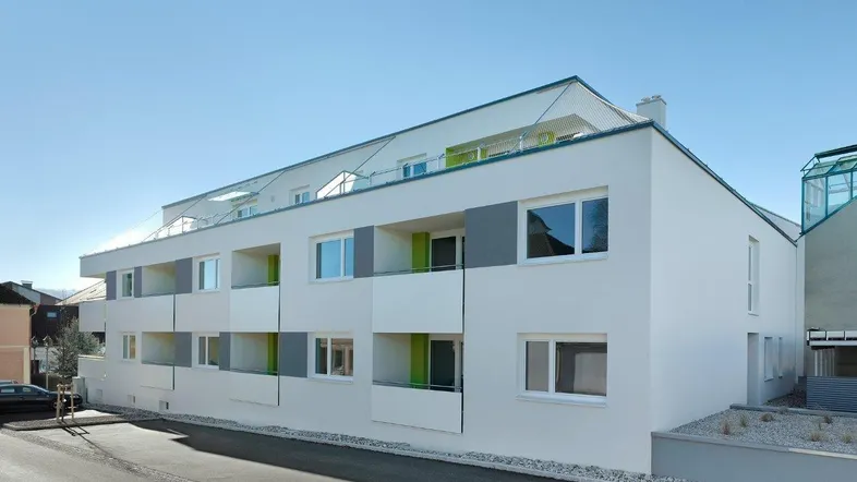 Moderne Wohnanlage mit weißer Fassade, grauen Akzenten und Balkonen unter blauem Himmel.