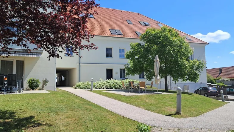 Wohngebäude mit rotem Ziegeldach, weißer Fassade und einem Gemeinschaftsgarten mit Sitzbereich.