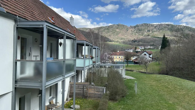Mehrere Balkone an einem Wohngebäude mit moderner Architektur und weitem Blick auf grüne Hügel.