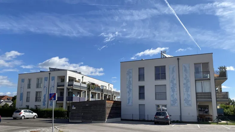 Zwei moderne Mehrfamilienhäuser mit Balkonen und Außenparkplätzen unter blauem Himmel.