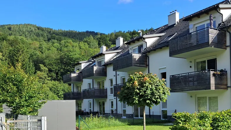 Moderne Wohnanlage mit mehreren Balkonen und Blick auf die bewaldeten Hügel.