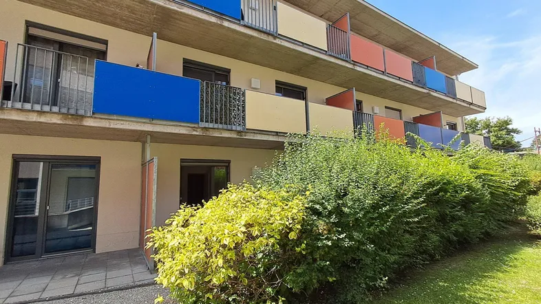 Mehrstöckiges Gebäude mit farbigen Balkonen und gepflegter Grünanlage im Vordergrund unter blauem Himmel.