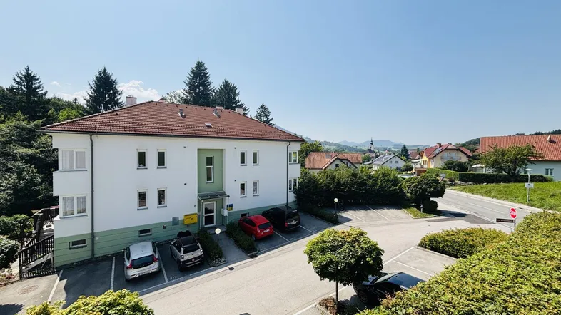Mehrfamilienhaus mit Parkplätzen und Blick auf die umliegende Landschaft und ein Dorf.