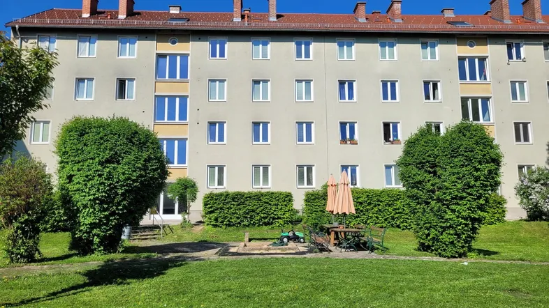Mehrstöckiges Wohngebäude mit großem Gemeinschaftsgarten, Sandkasten und Sitzgelegenheiten im Freien.