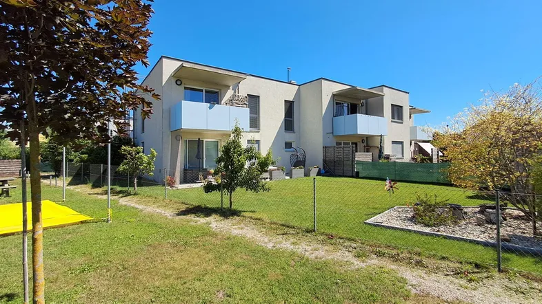 Moderne Mehrfamilienhäuser mit Balkonen und einem gepflegten Gemeinschaftsgarten unter blauem Himmel.