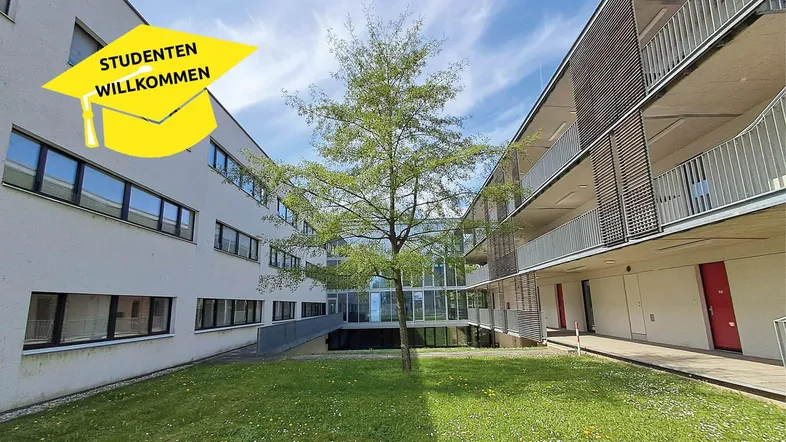 Moderner Gebäudekomplex mit begrüntem Innenhof und einem Baum in der Mitte.