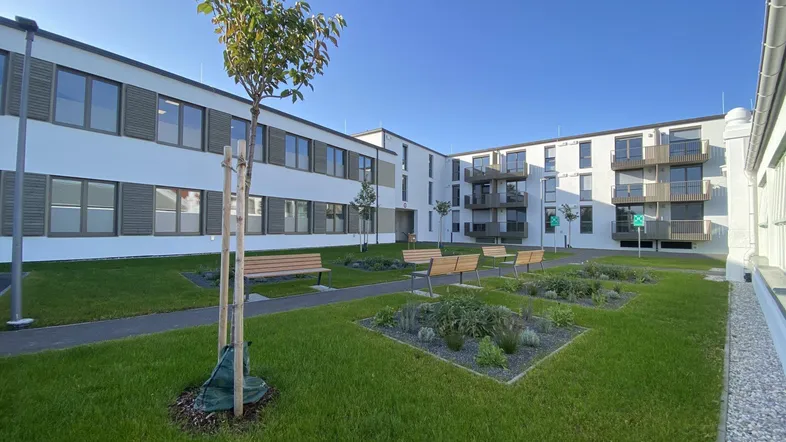 Moderner Apartmentkomplex mit gepflegtem Innenhofgarten und Sitzbänken unter blauem Himmel.