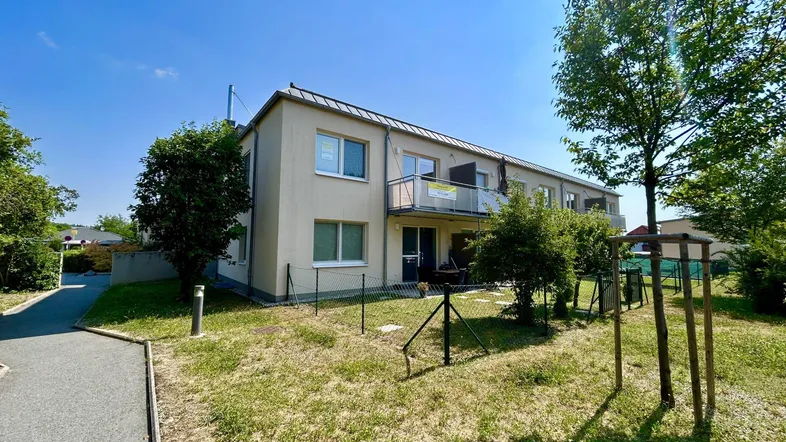 Mehrfamilienhaus mit Balkonen und Grünfläche unter blauem Himmel an einem sonnigen Tag.