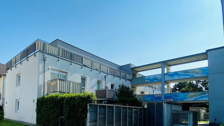 Modernes Mehrfamilienhaus mit Balkonen und begrünten Außenbereichen unter blauem Himmel.