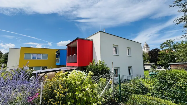 Moderne Wohnanlage mit farbigen Fassaden und gepflegtem Vorgarten unter blauem Himmel.