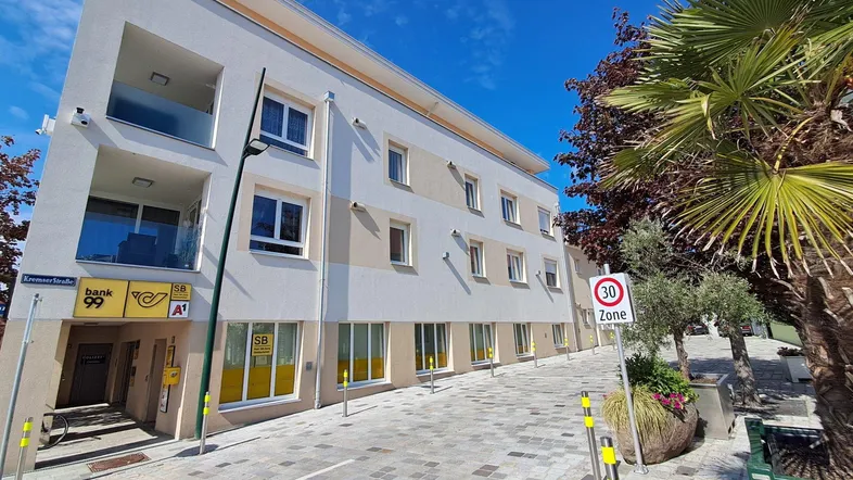 Modernes Mehrfamilienhaus mit Geschäften im Erdgeschoss und Wohnungen darüber, an einer gepflasterten Straße gelegen.