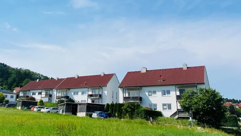Mehrere Wohngebäude mit roten Dächern und Balkonen, eingebettet in eine grüne Hügellandschaft.