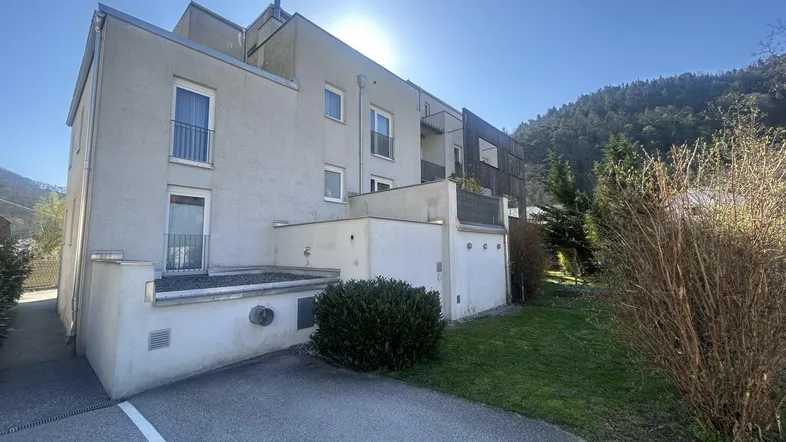 Modernes Mehrfamilienhaus mit Balkonen und grüner Umgebung unter strahlendem Himmel.