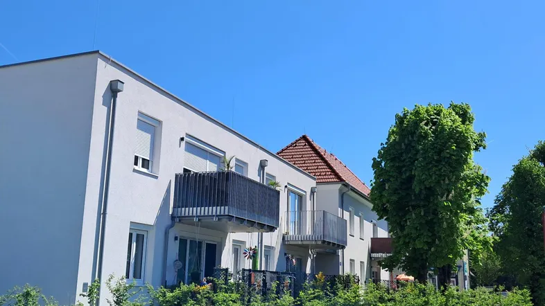 Modernes Mehrfamilienhaus mit Balkonen und gepflegter Hecke unter blauem Himmel.