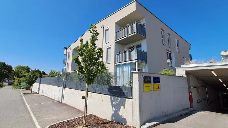Modernes Mehrfamilienhaus mit Balkonen und Zufahrt zur Tiefgarage unter strahlend blauem Himmel.