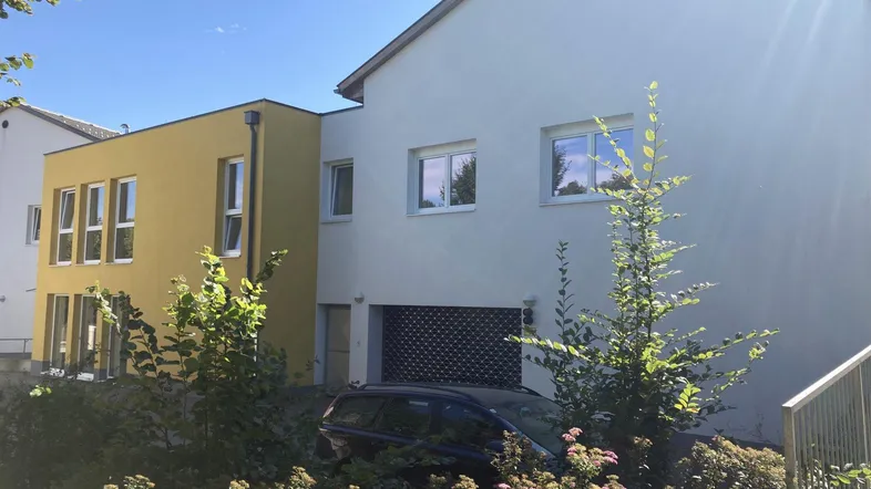 Ansicht der modernen Wohnanlage mit gelben Akzenten und umgebender Grünfläche unter blauem Himmel.