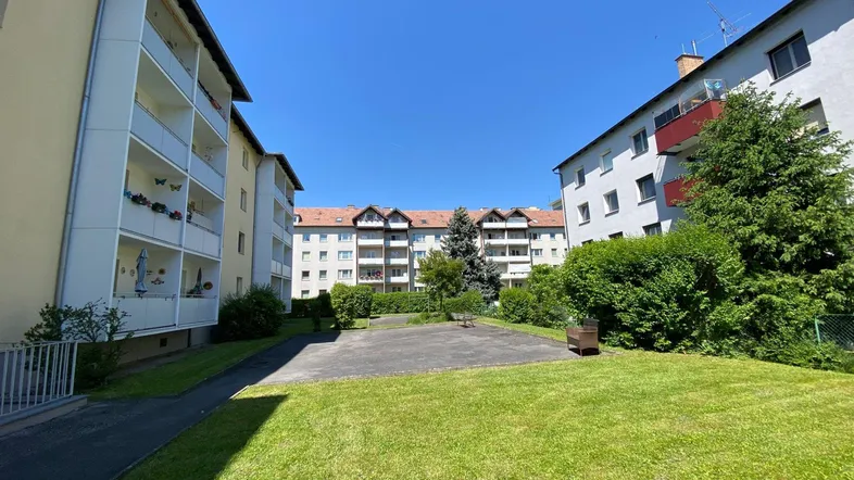 Blick auf die Wohnanlage mit begrüntem Innenhof und umliegenden Gebäuden unter blauem Himmel.