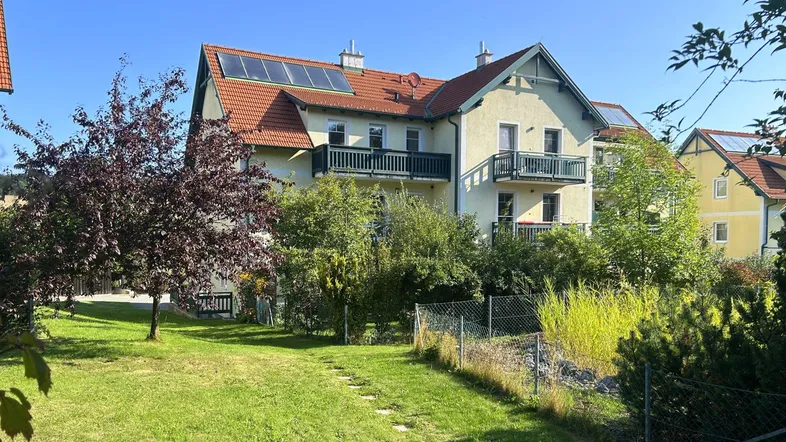Großzügiges Haus mit mehreren Balkonen, umgeben von einem grünen Garten und mit Solaranlage auf dem Dach.