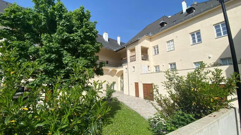 Innenhof eines Wohnkomplexes mit gepflastertem Weg und grünen Büschen unter blauem Himmel.