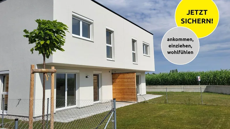 Modernes Reihenhaus mit weißer Fassade, Holzdetails und kleinem Vorgarten unter blauem Himmel.