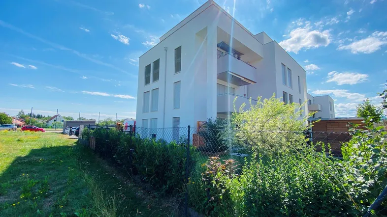 Modernes weißes Mehrfamilienhaus mit Balkonen unter strahlend blauem Himmel und Sonnenschein.