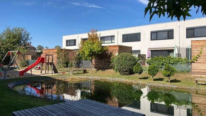Gepflegter Gartenbereich mit Teich, Spielplatz und Blick auf die moderne Wohnanlage.