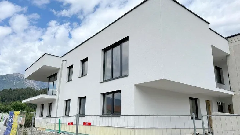 Modernes weißes Gebäude im Bau mit großen Fenstern und Balkonen vor einer Bergkulisse.