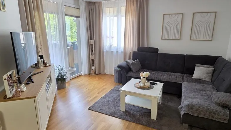 Helles Wohnzimmer mit gemütlichem Sofa, Holzboden und Zugang zum Balkon, modern eingerichtet.