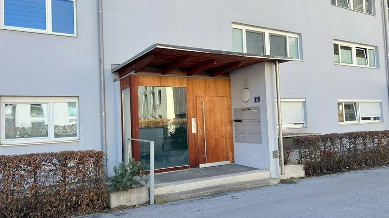 Eingangsbereich eines Mehrfamilienhauses mit Holztür und Vordach.