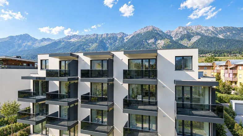 Moderne Wohnanlage mit Balkonen und Bergblick unter blauem Himmel.