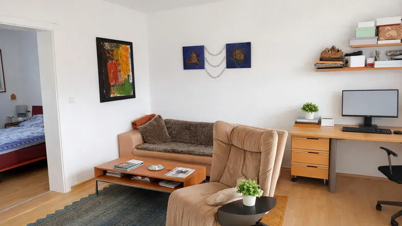 Helles Wohnzimmer mit Sofa, Schreibtisch und Zugang zu einem angrenzenden Schlafzimmer.