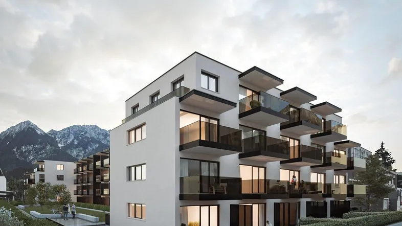 Moderne Wohnanlage mit Balkonen und Tiefgaragenzufahrt vor alpiner Bergkulisse.