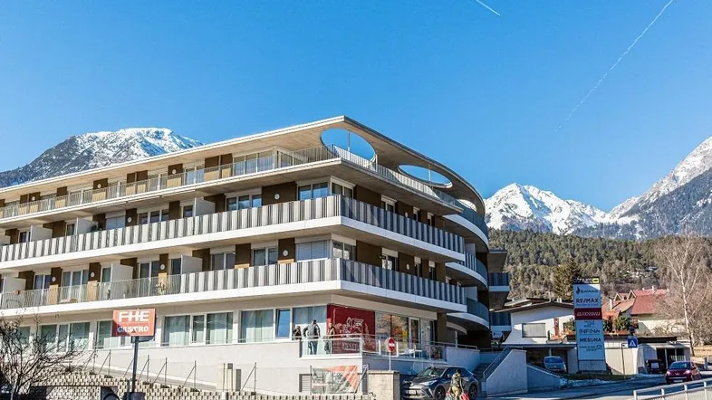 Modernes Mehrfamilienhaus mit Balkonen und Blick auf die schneebedeckten Berge.